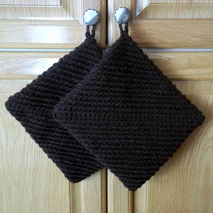 May include: Two brown crocheted pot holders with loops for hanging. The pot holders are hanging on cupboard doors.