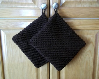 May include: Two brown crocheted pot holders with loops for hanging. The pot holders are hanging on cabinet doors.