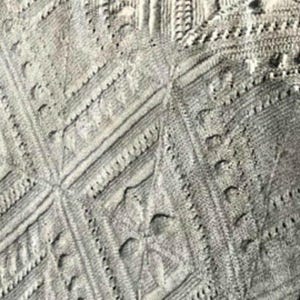 May include: Close-up of a gray knitted fabric with a textured diamond pattern.