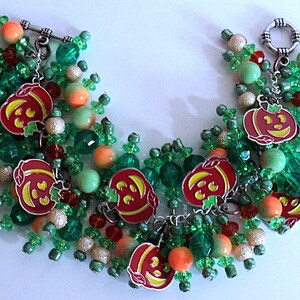 May include: A Halloween-themed beaded bracelet. It features red pumpkin charms with yellow faces, mixed with green, orange, and silver beads. The bracelet is fastened with a silver toggle clasp.