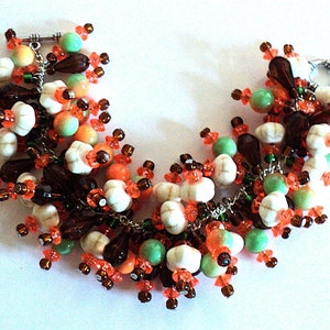 May include: A multi-coloured beaded bracelet featuring white, brown, orange and green beads. The bracelet is made with a variety of different bead shapes and sizes.