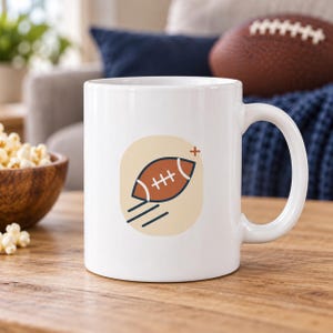 Peut inclure: Un mug en céramique blanche orné d'un motif graphique représentant un ballon de football américain marron centré dans un carré aux coins arrondis de couleur beige clair. Le ballon présente des lacets blancs et des lignes de mouvement bleu foncé.