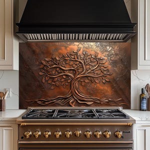 May include: A copper-colored backsplash featuring a detailed relief of a tree with roots and leaves. The artwork is mounted above a gas range with brass-colored knobs, set against a neutral kitchen backdrop.