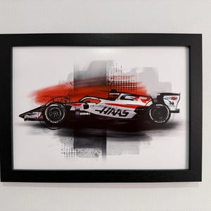 May include: Framed art print of a Formula 1 race car. The car is white and red, with black wheels and accents. The background has abstract red and grey brushstrokes, and the frame is black.