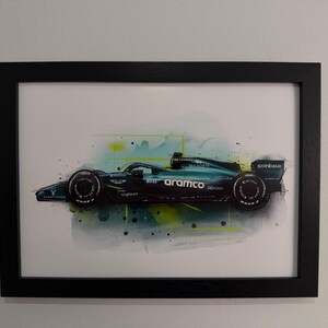 May include: Framed print of a Formula 1 race car in teal and black, with sponsor logos including "aramco" and "coinbase." The artwork features watercolor-style splashes of teal, yellow, and black. The print is in a black frame.