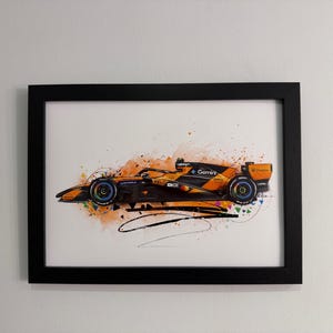 Può includere: Stampa artistica incorniciata di una macchina da corsa di Formula 1 arancione e nera, con accenti colorati. L'opera presenta uno stile acquerello con schizzi di vernice e dettagli di linee nere. L'auto è su sfondo bianco.