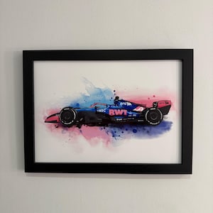 May include: Framed watercolour print of a Formula 1 race car in blue, pink, and black. The car is set against a backdrop of blue and pink watercolour splashes. The frame is black.