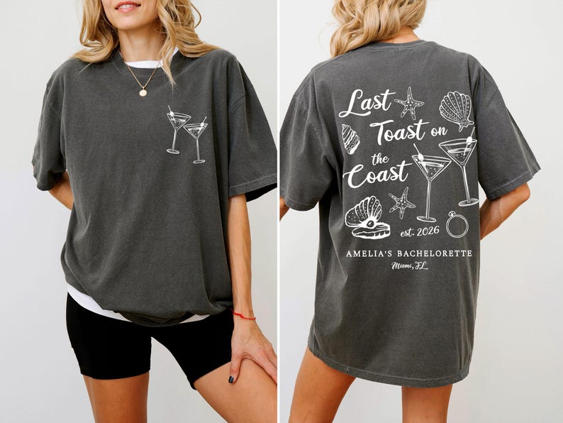 K&ouml;nnte beinhalten: Dunkelgraues T-Shirt mit wei&szlig;er Grafik von zwei Martinigl&auml;sern auf der Vorderseite. Auf der R&uuml;ckseite steht der Text "Last Toast on the Coast" mit Muscheln, Seesternen, Martinigl&auml;sern und einem Ring. Mit "Amelia's Bachelorette" und "Miami, FL".