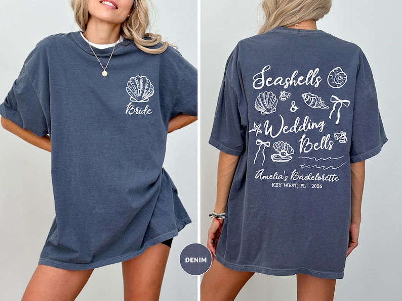 K&ouml;nnte beinhalten: Denimblaues T-Shirt mit wei&szlig;er Muschel und "Bride"-Text auf der Vorderseite. Die R&uuml;ckseite zeigt den Text "Seashells & Wedding Bells" und Illustrationen. Amelia's Bachelorette, Key West, FL, 2026.