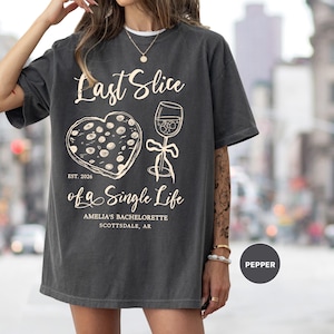 Puede incluir: Camiseta gris oscuro con el texto "Last Slice of a Single Life" y un gráfico de una porción de pizza y una copa de vino. El texto "Amelia's Bachelorette Scottsdale, AR" también está impreso en la camiseta.