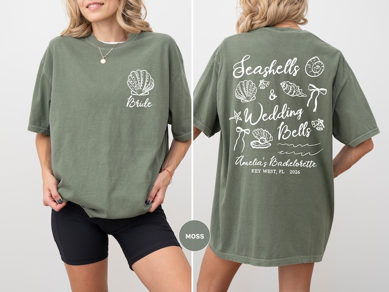 K&ouml;nnte beinhalten: Moosgr&uuml;nes T-Shirt mit einem Muschelmuster und dem Wort "Bride" auf der Vorderseite. Auf der R&uuml;ckseite des Shirts befinden sich Muscheln, die Worte "Seashells & Wedding Bells" und "Amelia's Bachelorette, Key West, FL, 2026".