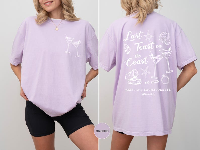 K&ouml;nnte beinhalten: Orchideenfarbenes T-Shirt mit wei&szlig;er Grafik von zwei Martinigl&auml;sern auf der Vorderseite. Auf der R&uuml;ckseite steht der Text "Last Toast on the Coast" mit Muschel- und Ringillustrationen. "Amelia's Bachelorette" ist ebenfalls auf der R&uuml;ckseite aufgedruckt.