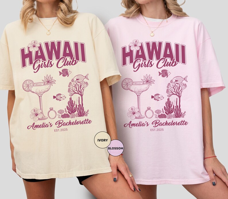 K&ouml;nnte beinhalten: Zwei &uuml;bergro&szlig;e T-Shirts, eines in Elfenbein und eines in Rosa, mit einem lila Aufdruck. Der Aufdruck lautet "HAWAII Girls Club" &uuml;ber einem Cocktail-, Fisch- und Korallen-Design. Darunter steht "Amelia's Bachelorette EST.2025".
