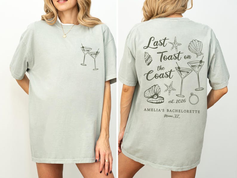 K&ouml;nnte beinhalten: Hellgr&uuml;nes T-Shirt mit Front- und R&uuml;ckendesign. Die Vorderseite zeigt zwei Martinigl&auml;ser. Auf der R&uuml;ckseite steht "Last Toast on the Coast" mit Muschel- und Seestern-Grafiken sowie "Amelia's Bachelorette Miami, FL".