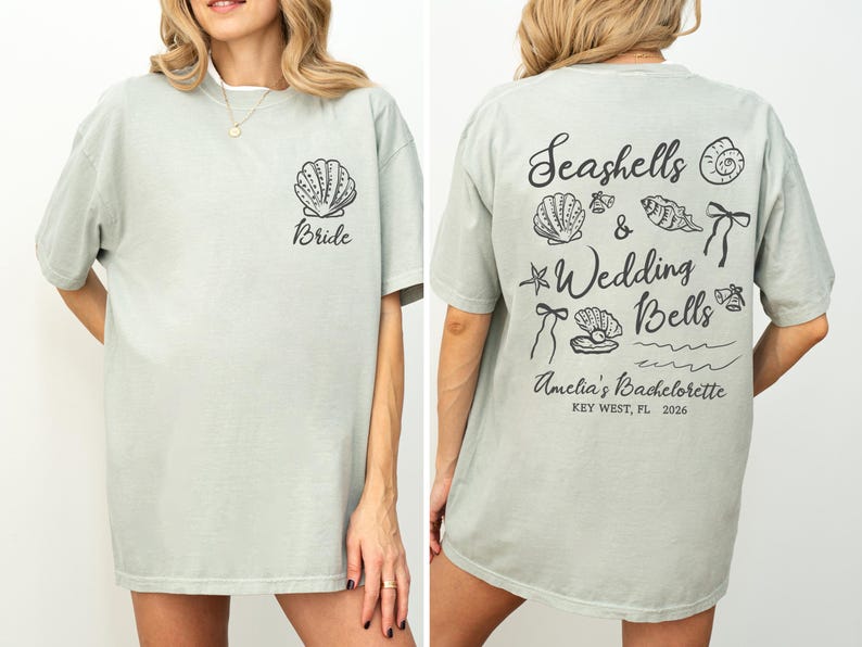 K&ouml;nnte beinhalten: Hellgr&uuml;nes T-Shirt mit einer Muschel und dem Wort "Bride" auf der Vorderseite. Auf der R&uuml;ckseite des Shirts steht "Seashells & Wedding Bells" mit Muschel- und Glockenillustrationen. Das Shirt ist f&uuml;r einen Junggesellinnenabschied in Key West, FL.