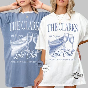 May include: Two oversized t-shirts, one blue jean and one white, featuring a graphic design. The design includes the text "THE CLARKS LAKE CLUB" with a boat, champagne glasses, and the text "EST. 2025". The text "AMELIA'S BACHELORETTE" is also included.