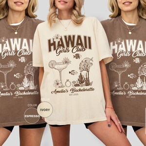 K&ouml;nnte beinhalten: Espresso- und elfenbeinfarbene T-Shirts mit dem Text "HAWAII Girls Club" im Vintage-Stil. Die Shirts zeigen ein tropisches Design mit einem Cocktail, Fischen und Korallen. Der Text "Amelia's Bachelorette EST. 2025" ist ebenfalls aufgedruckt.