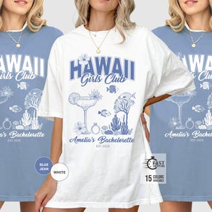 K&ouml;nnte beinhalten: Wei&szlig;e oder blau-Jeans-T-Shirts mit blau-wei&szlig;em Grafikdesign. Das Design enth&auml;lt den Text "HAWAII Girls Club" und "Amelia's Bachelorette EST. 2025" sowie Illustrationen eines Cocktails, Fisches und Korallen.