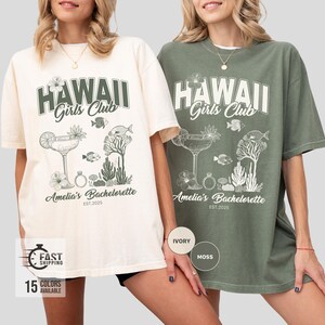 K&ouml;nnte beinhalten: Elfenbein- und moosgr&uuml;ne T-Shirts mit einem grafischen Design. Das Design enth&auml;lt den Text "HAWAII Girls Club" &uuml;ber einem Cocktail, Fischen und floralen Elementen. Der Text "Amelia's Bachelorette EST.2025" steht darunter.