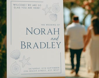 May include: A wedding welcome sign on a wooden easel. The sign is white with blue text that reads "WELCOME! WE ARE SO GLAD YOU ARE HERE!" and "THE WEDDING OF NORAH and BRADLEY". Includes seashell and starfish illustrations.