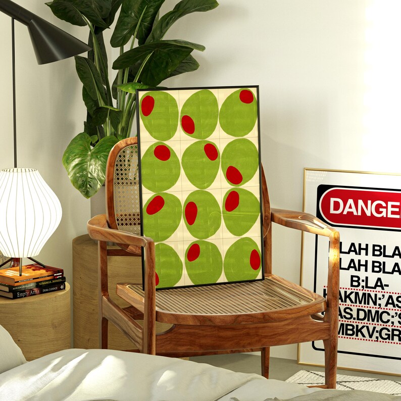 May include: A framed art print featuring a grid of green olives with red centers on a cream background. The artwork is displayed on a wooden chair. A sign with the word "DANGER" is visible in the background.