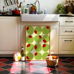 May include: A kitchen scene with a framed artwork featuring green circles with red centers. A bottle of wine, a bag of pasta, and a basket of fruit sit on the floor. The floor has a red and black diamond pattern.