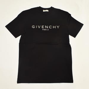 May include: Black short-sleeved t-shirt with the brand name "GIVENCHY PARIS" in silver lettering across the chest. The shirt has a crew neck and a simple, classic design, suitable for casual wear.