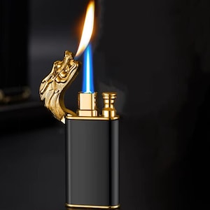 May include: A black and gold lighter with a dragon head design. The lighter has a blue flame and is lit.