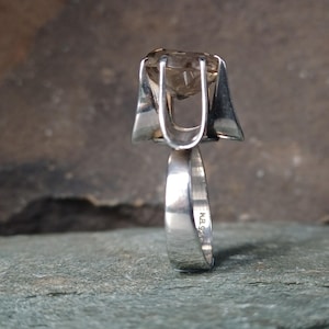 May include: A sterling silver ring featuring a large, faceted, light brown gemstone held in a high-profile, four-prong setting. The band is smooth and polished, with the hallmark N.B. 925 clearly visible on the inner surface of the metal shank.