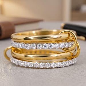 Anillo de moissanita de 1 quilate con múltiples bandas y aros entrelazados de oro amarillo; una joya llamativa.