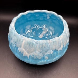 May include: A round, ceramic bowl with a light blue glaze and a textured, wavy rim. The interior is a solid light blue, while the rim features a white, textured pattern. The bowl is likely used for decorative purposes or as a small planter.
