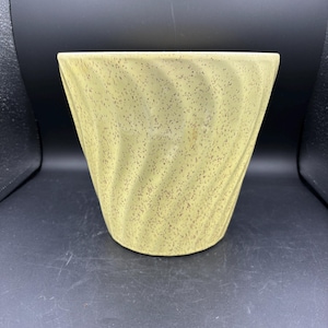 May include: A pale yellow ceramic planter with a speckled pattern and a flared, conical shape. The planter has a textured, swirled design and is suitable for indoor or outdoor use.