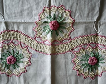 May include: White fabric with three crocheted floral designs. Each design features a pink flower with green leaves and a white crocheted border.