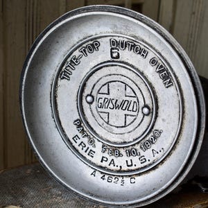 May include: A round, silver-toned metal lid for a Griswold Tite-Top Dutch Oven, size 6. The surface features embossed text reading TITE-TOP DUTCH OVEN, GRISWOLD, PAT'D. FEB. 10, 1920, ERIE PA., U.S.A., and the alphanumeric code A 462 1/2 C.
