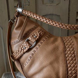 Pu&ograve; includere: Una borsa in pelle marrone con manico e tracolla intrecciati. La borsa presenta un design intrecciato sul davanti e cuciture decorative. Dettagli in metallo argentato impreziosiscono il design della borsa.