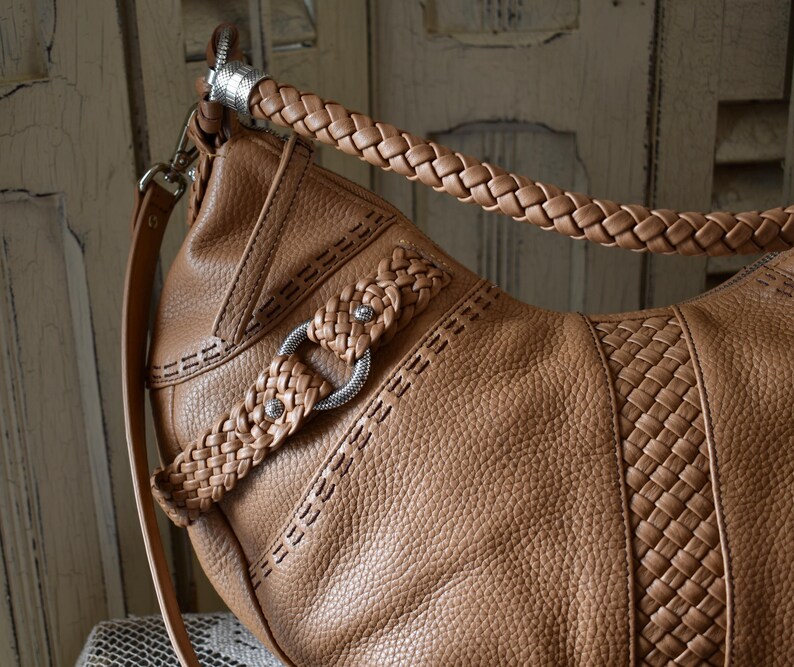 Pu&ograve; includere: Una borsa in pelle marrone con manico e tracolla intrecciati. La borsa presenta un design intrecciato sul davanti e cuciture decorative. Dettagli in metallo argentato impreziosiscono il design della borsa.