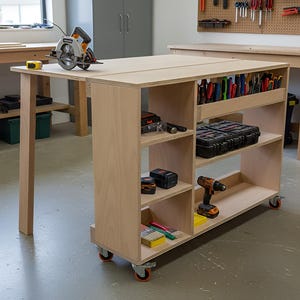 Op de afbeelding: Een lichtgekleurde houten werkbank met een cirkelzaag erop. De werkbank heeft planken en opbergruimte voor gereedschap, waaronder een boormachine, schroevendraaiers en een gereedschapskist. De werkbank staat op wielen en staat in een werkplaats.