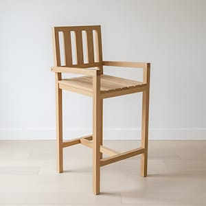 Peut inclure: Un tabouret de bar en bois clair avec une assise et un dossier à lattes. Le tabouret est doté d'accoudoirs et d'un repose-pieds, et est construit avec des lignes droites et un design minimaliste. La chaise est en bois clair et repose sur un sol en bois clair.