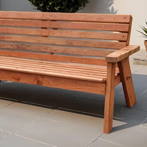 K&ouml;nnte beinhalten: Eine Gartenbank aus Holz mit Lattenr&uuml;cken und -sitzfl&auml;che. Die Bank ist aus rotbraunem Holz gefertigt und hat Armlehnen. Eine Topfpflanze steht in der N&auml;he auf einer Steinoberfl&auml;che. Die Bank ist f&uuml;r Sitzgelegenheiten im Freien konzipiert.