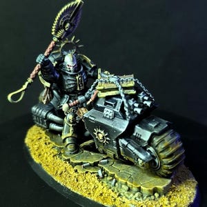 May include: A detailed miniature of a warrior riding a black motorcycle. The warrior is clad in black armor and wields a large weapon. The motorcycle has a rugged design with a skull emblem. The base is textured with a yellow-brown color.