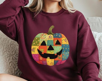 Op de afbeelding: Bordeaux sweatshirt met een patchwork pompoen ontwerp. De pompoen heeft een lachend gezicht en is gemaakt van kleurrijke stoffen vierkanten met bloempatronen. De sweatshirt is een comfortabele, casual stijl, perfect voor de herfst en Halloween.