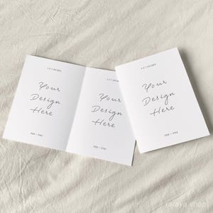May include: A white folded card with the text "Your Design Here" on each side. The card is 3.5 x 5 inches and is on a beige fabric background.
