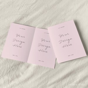 May include: A tri-fold card mockup with a pink background. The card is 3.5 x 5 inches and has the text "Your Design Here" on each panel. The card is lying flat on a white fabric surface.
