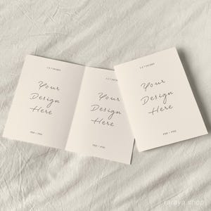May include: A folded card mockup with three panels. Each panel has the text "Your Design Here" and the dimensions "3.5 x 5 inches" printed on it. The card is on a white fabric background.