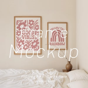 May include: Two framed art prints with wooden frames. One print says "GOOD VIBES" with floral designs in pink. The other print says "FOLLOW THE RAINBOW" with a pink rainbow design. A brown vase with branches sits on a wooden table.