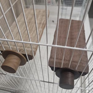 以下が含まれることがあります： 木製の鳥かご用止まり木が2つ。1つは薄茶色、もう1つは濃い茶色です。各止まり木には、ケージに取り付けるための円筒形のベースが付いています。止まり木は白いワイヤーケージの中にあります。