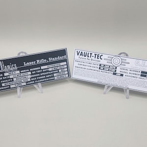 May include: Two metal plates with black and white text. The top plate is black with white text and says "General Atomics Laser Rifle, Standard". The bottom plate is white with black text and says "VAULT-TEC Future-Tec Division".