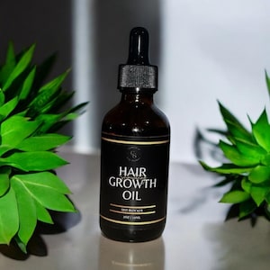 May include: A dark brown glass bottle of hair growth oil with a black label and gold trim. The label reads "Hair Growth Oil" and "DHT Blocker". The bottle has a black dropper and contains 2 fl oz (59ml).