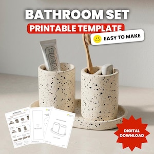 Puede incluir: Un conjunto de baño con plantilla imprimible que incluye dos soportes cilíndricos de color crema con motas y una bandeja ovalada. Un soporte contiene un tubo de pasta de dientes y el otro un cepillo de dientes de madera. Incluye hojas de instrucciones.