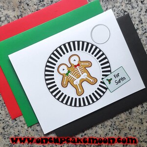 May include: A white card with a black and white striped circle containing two gingerbread men skeletons with bow ties. The card says "For Santa" in a green box with a holly sprig.